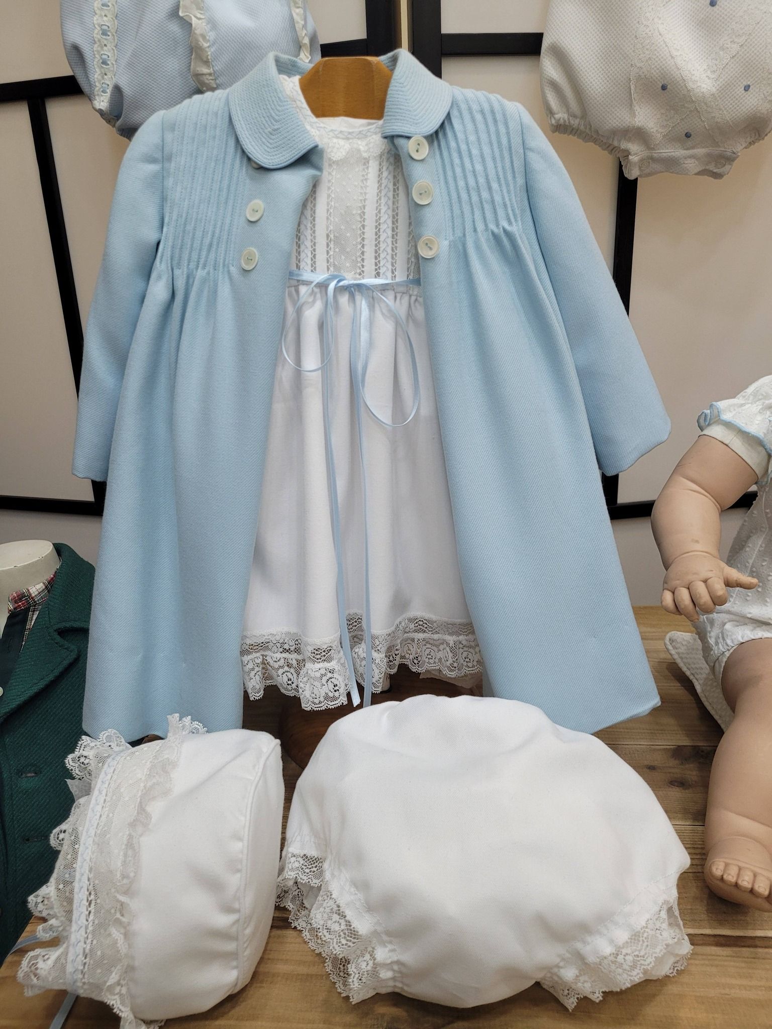 Conjunto de abrigo y vestido azul para bebé con gorro y capota a juego, expuesto en percha.