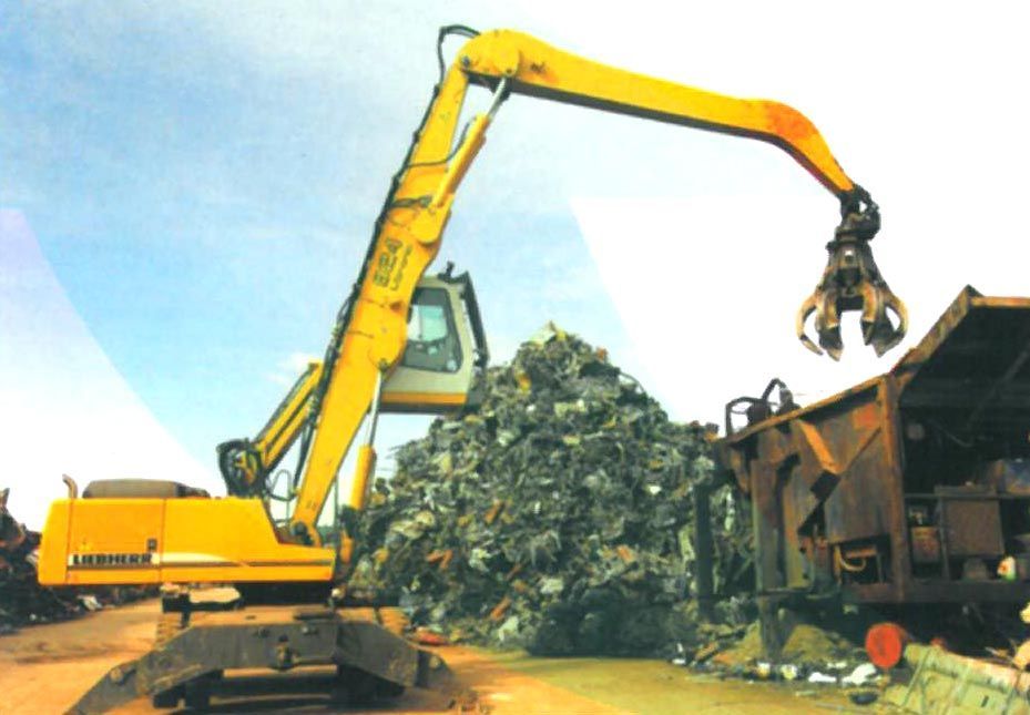 Excavadora amarilla cargando chatarra en un camión en un desguace.
