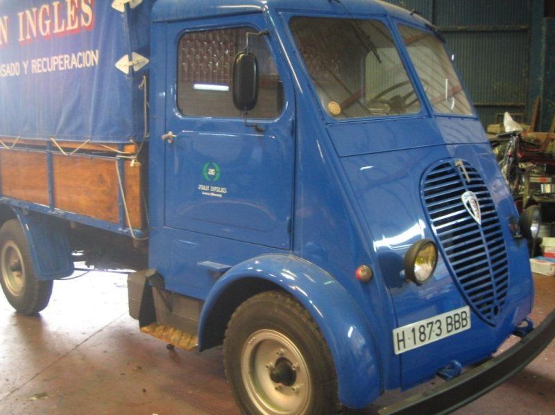 Furgoneta de reparto azul de estilo clásico con letras naranjas aparcada en el interior.