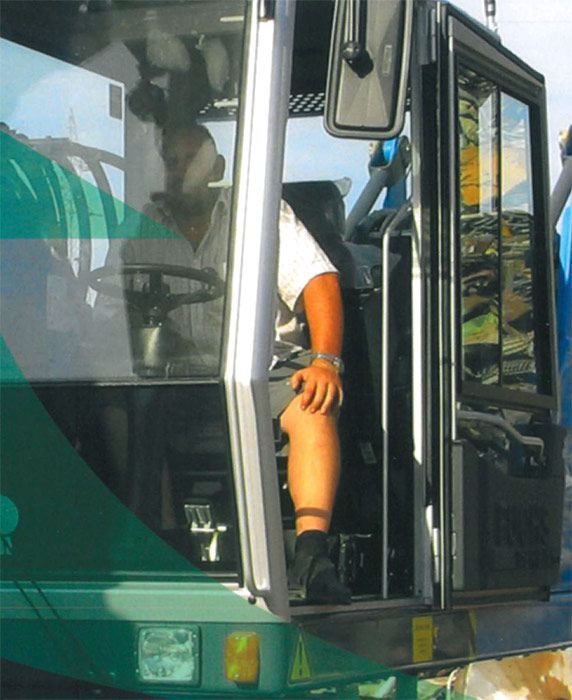 Conductor de autobús sentado en la puerta abierta de un autobús verde, con la mano sobre la rodilla.
