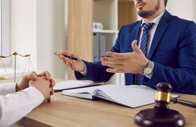 Un hombre con traje y corbata está sentado en un escritorio hablando con otro hombre.