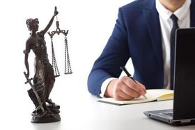 Un hombre escribe en un cuaderno junto a una estatua de la justicia.