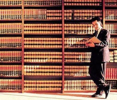 Un hombre con traje está leyendo un libro en una biblioteca.