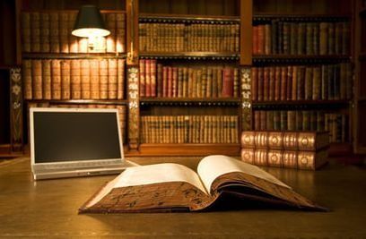 Un libro abierto y una computadora portátil están sobre un escritorio en una biblioteca.