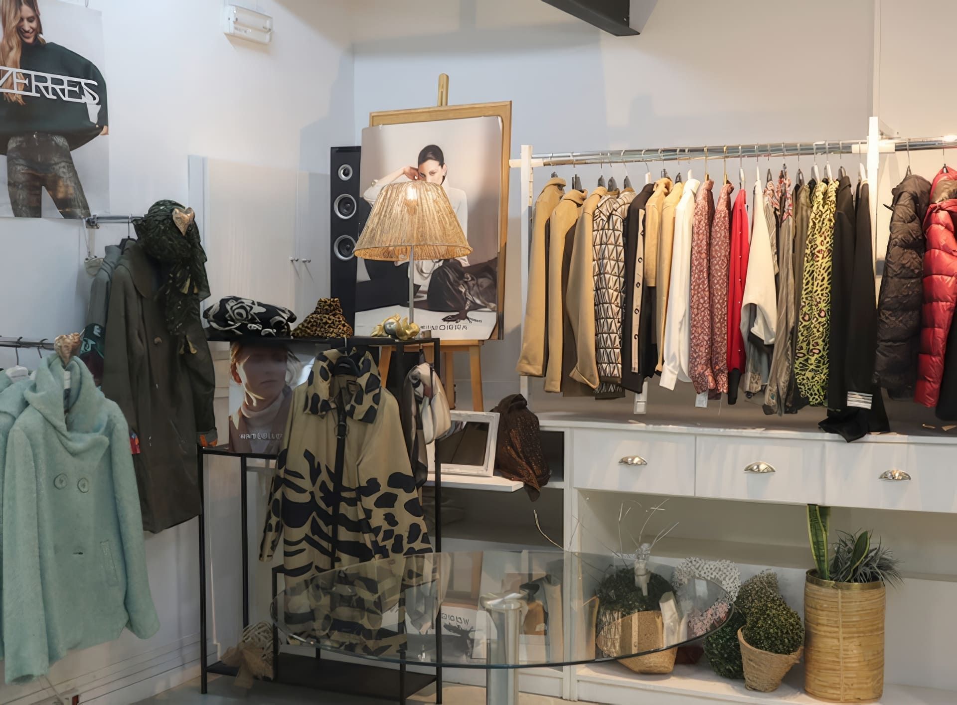 Percheros de ropa en una boutique: abrigos, suéteres, vestidos. Iluminación tenue y obras de arte.