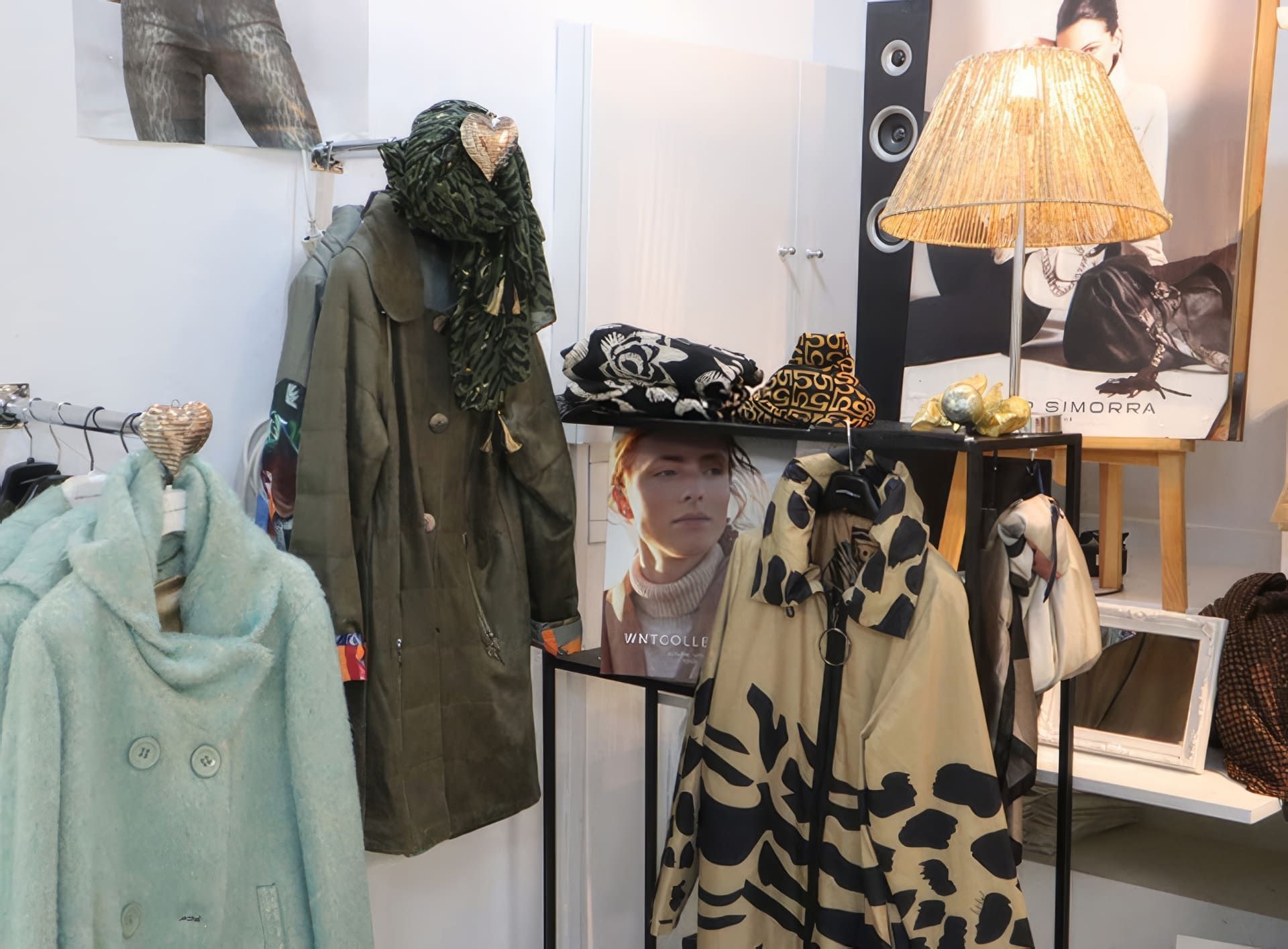 Exhibición de una tienda de ropa: abrigos colgados en percheros, una lámpara y un cartel.