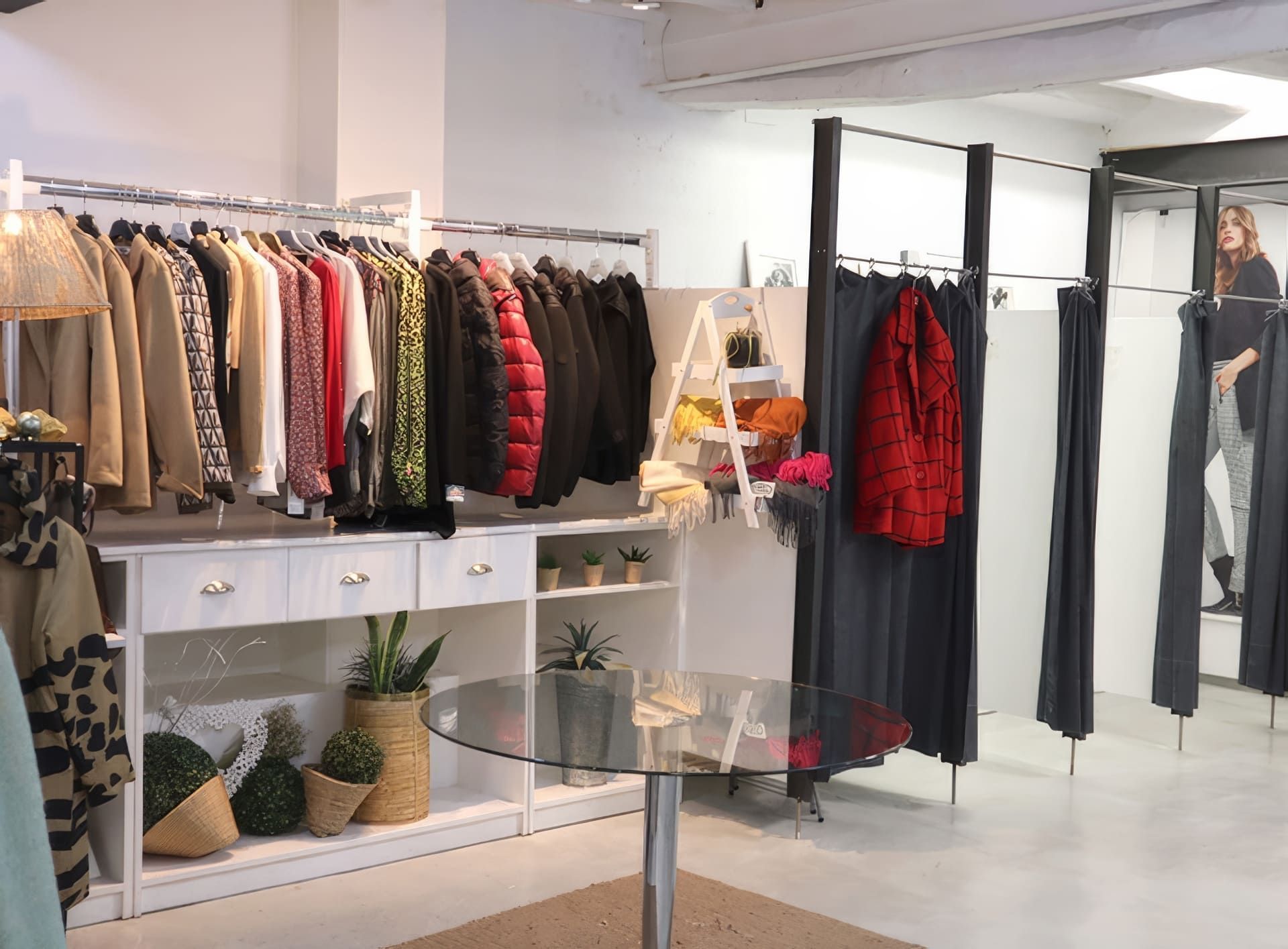 Interior de tienda de ropa con estantes de ropa, probadores y un cliente en uno.