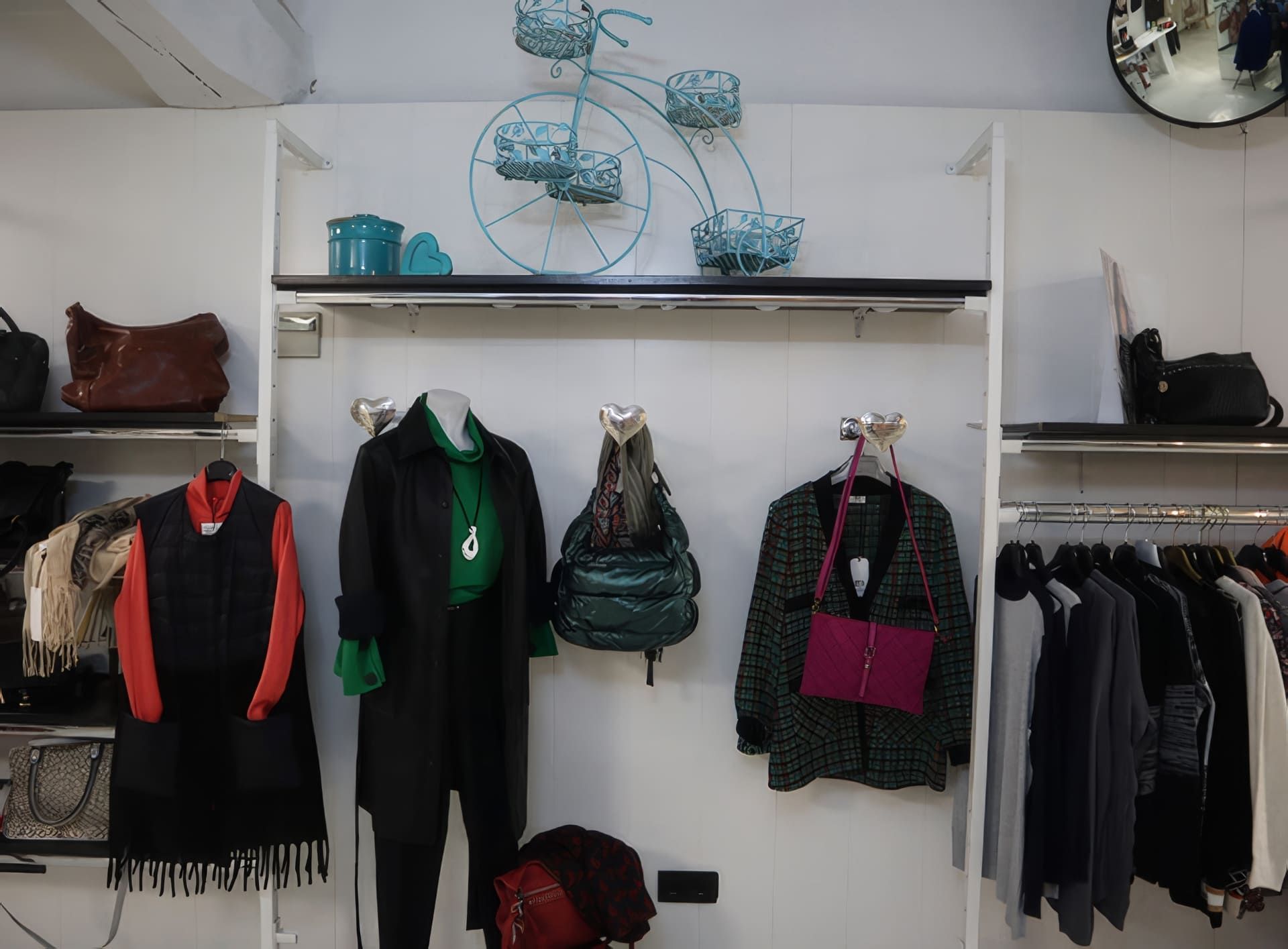 Exhibición de tienda de ropa con maniquí con abrigo, bolsos, chaquetas colgadas y decoración.