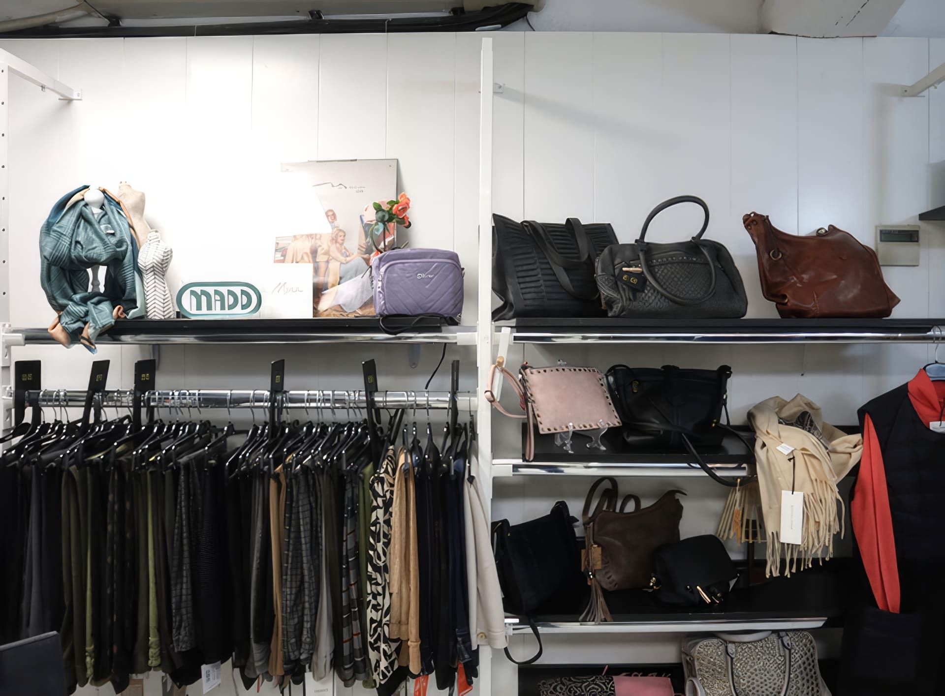 Exhibición de tienda de ropa con pantalones en perchas y bolsos en estantes.