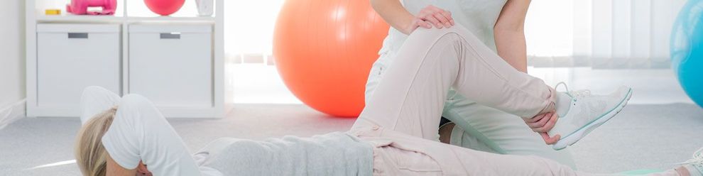 Eine Frau streckt in einem Fitnessstudio die Beine einer anderen Frau.