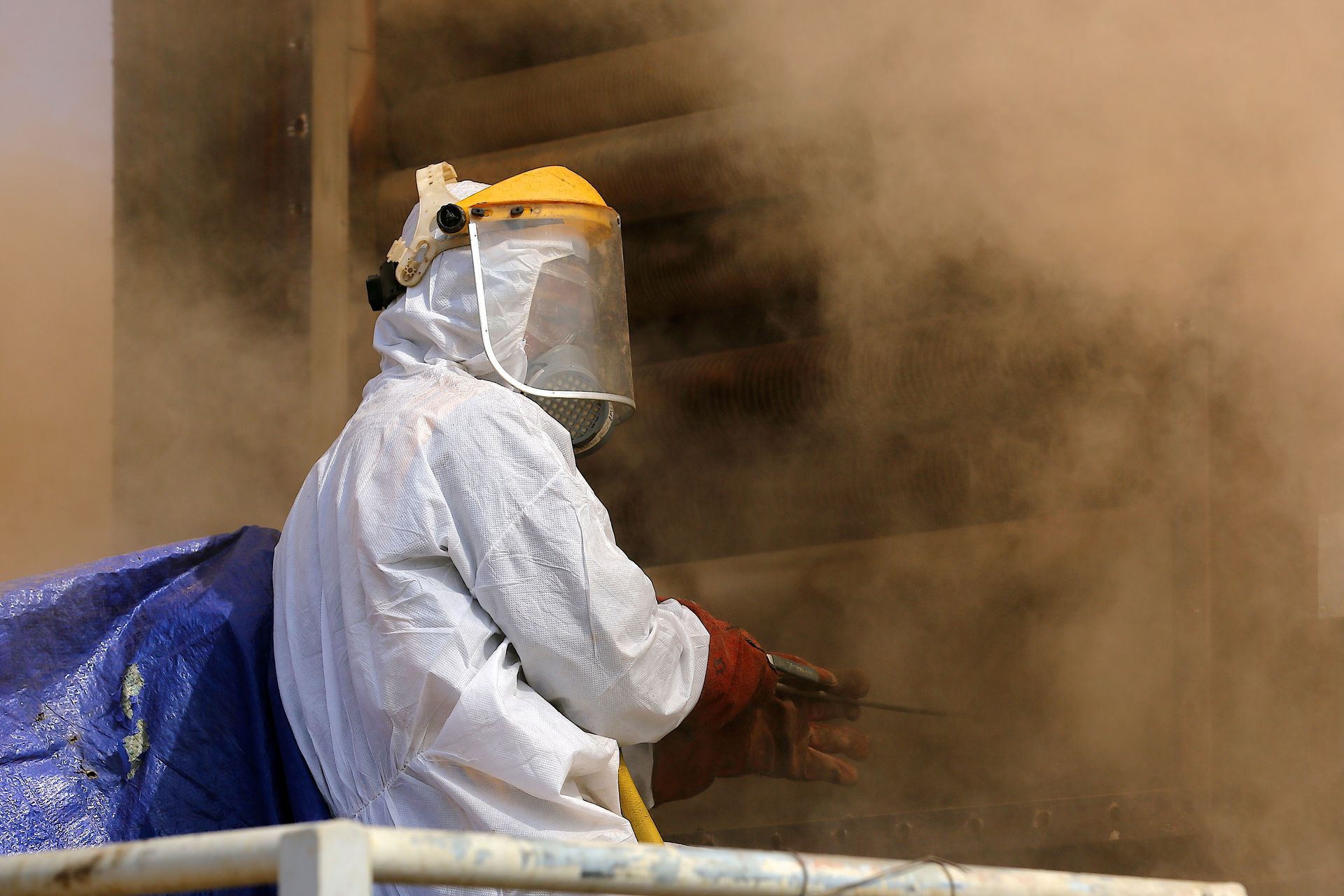 Personne en combinaison de protection utilisant un outil, masquée par la poussière/fumée, à l'extérieur.
