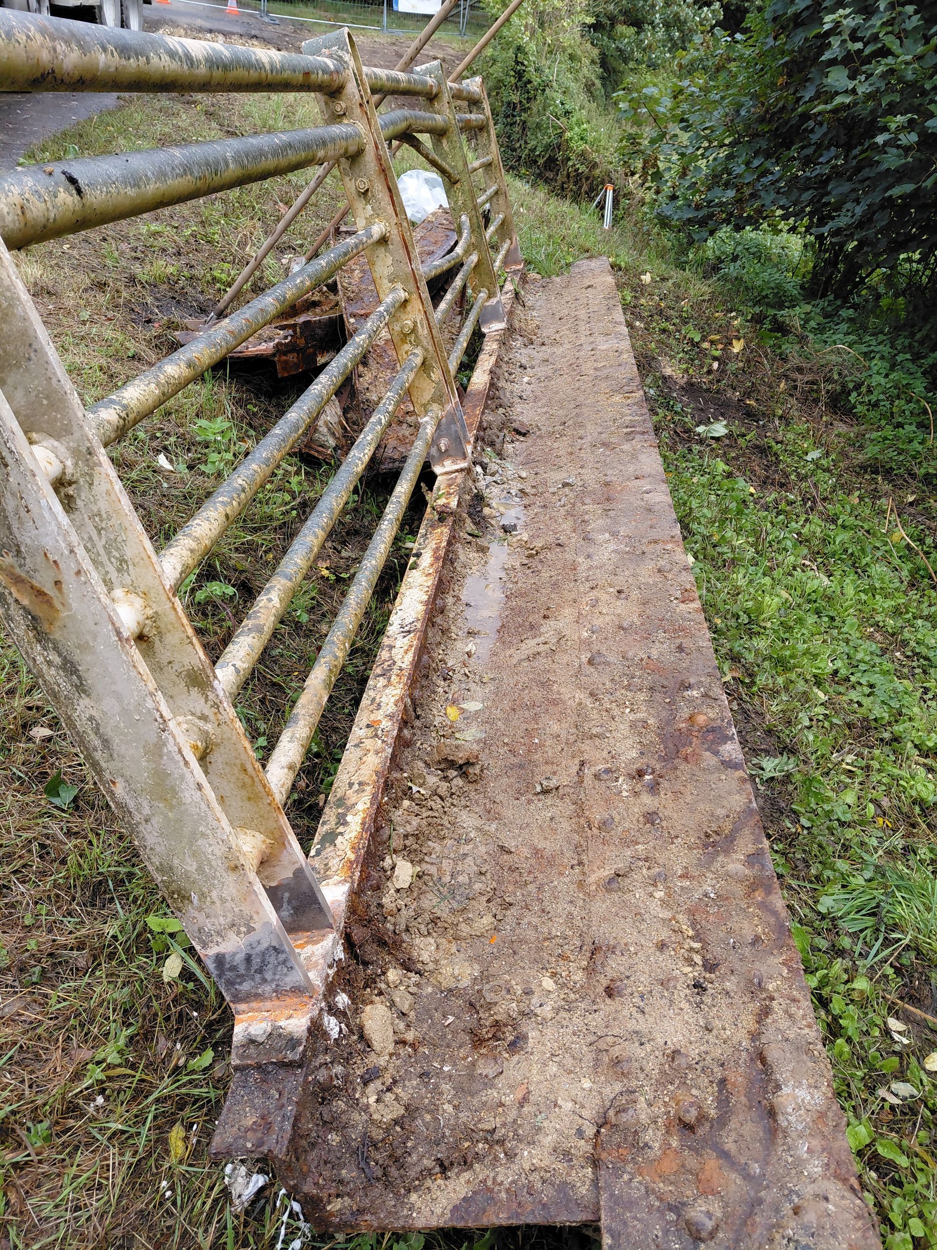 Un portail métallique rouillé gît sur une dalle de béton délabrée, à côté d'une zone herbeuse.