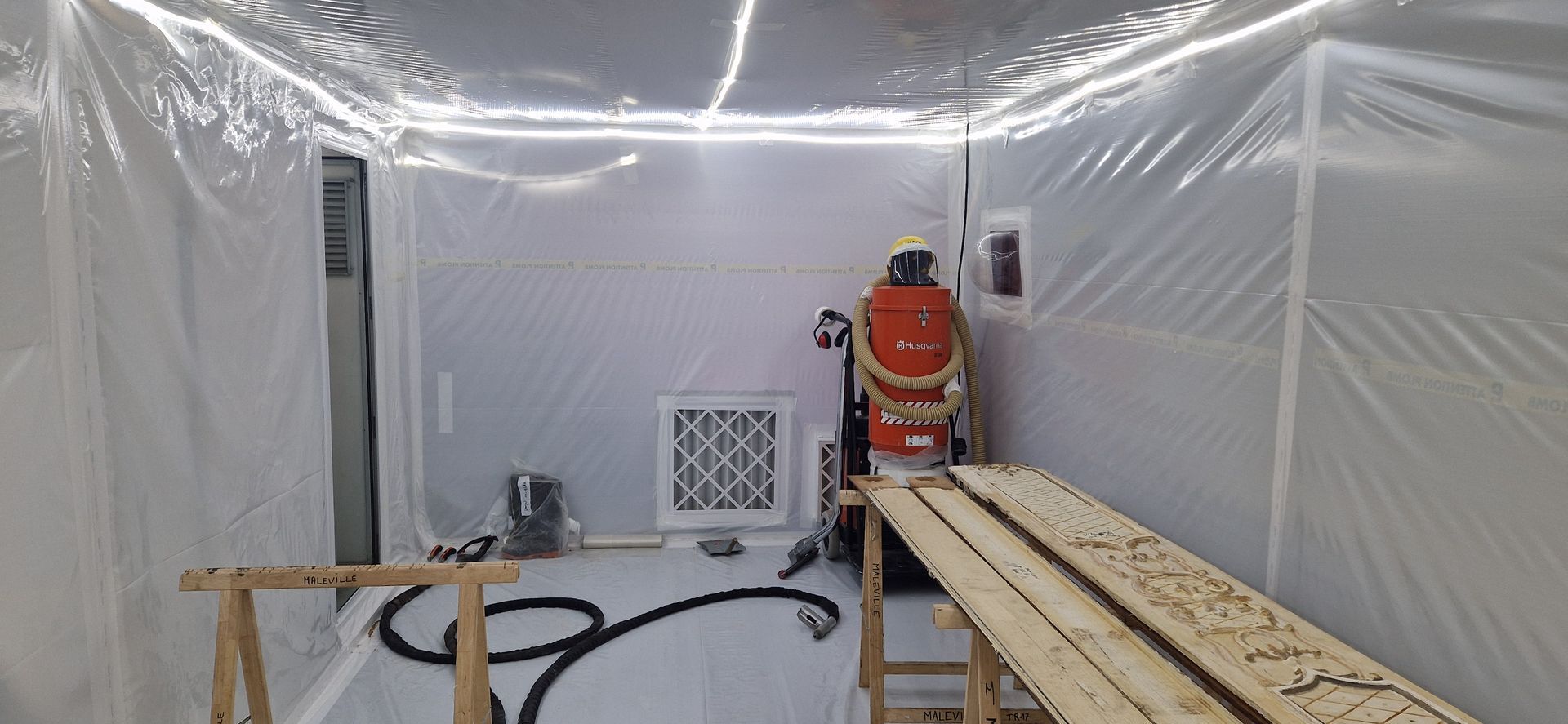 Une personne ponce du bois à l'intérieur d'une enceinte en plastique transparent.