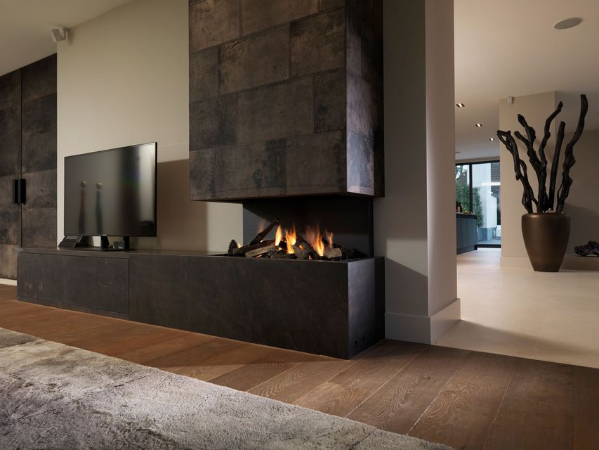 Salon moderne avec cheminée en pierre sombre et flammes, télévision à écran plat, parquet et plante décorative.