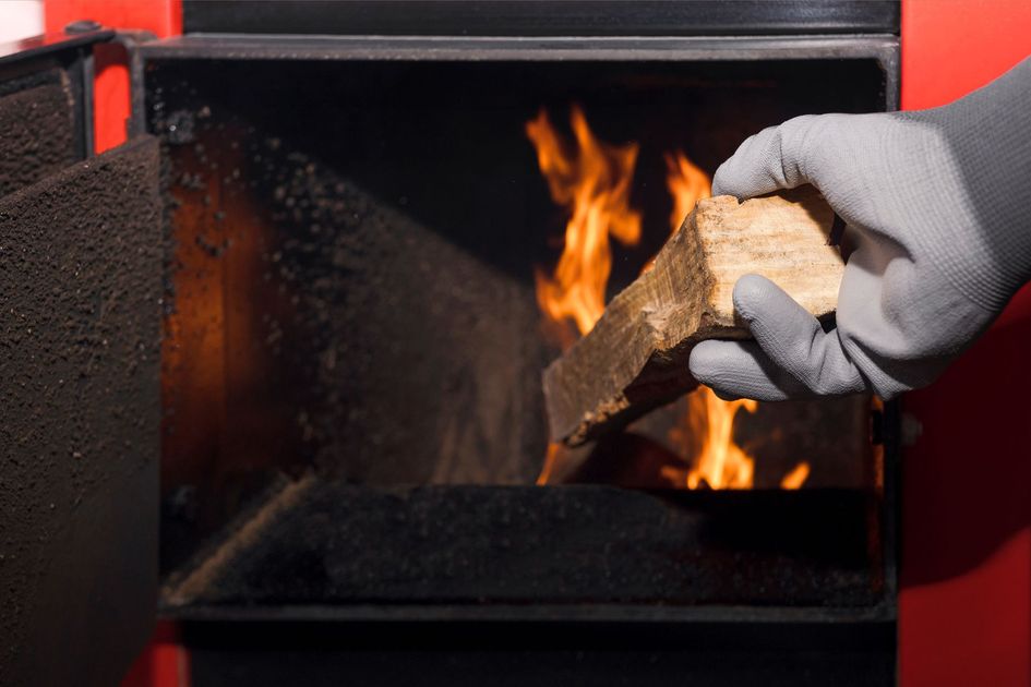 Une main gantée place un morceau de bois dans les flammes d'une cheminée ou d'un four.