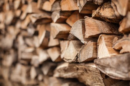 Gros plan en biais d'une pile de bûches fendues soigneusement empilées, mettant en valeur les différentes textures et les tons chauds du bois.