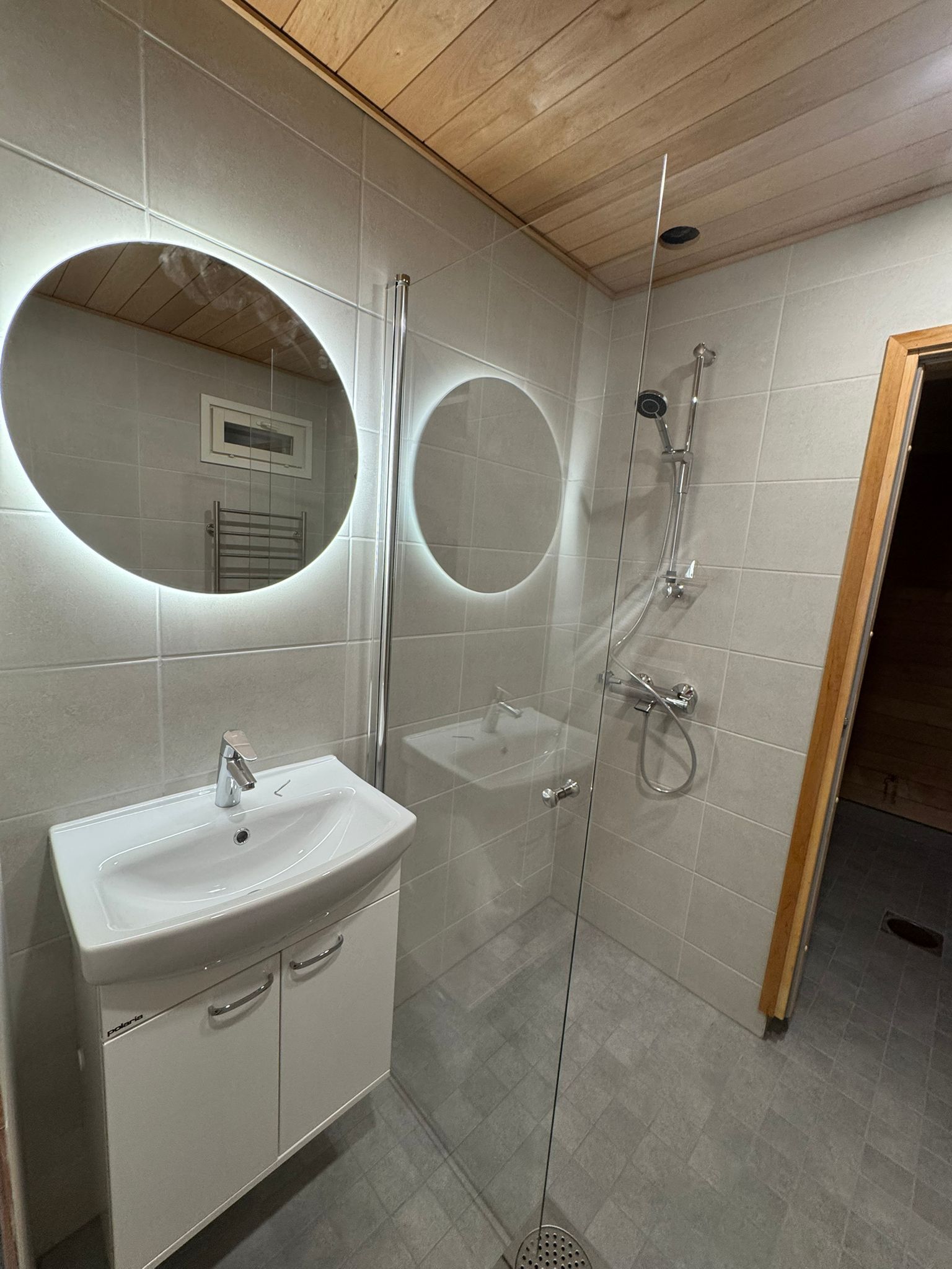 Renomen Oy kylpyhuoneremontti Uusimaa moderni pyöreä valopeili ja valkoinen allaskaappi.