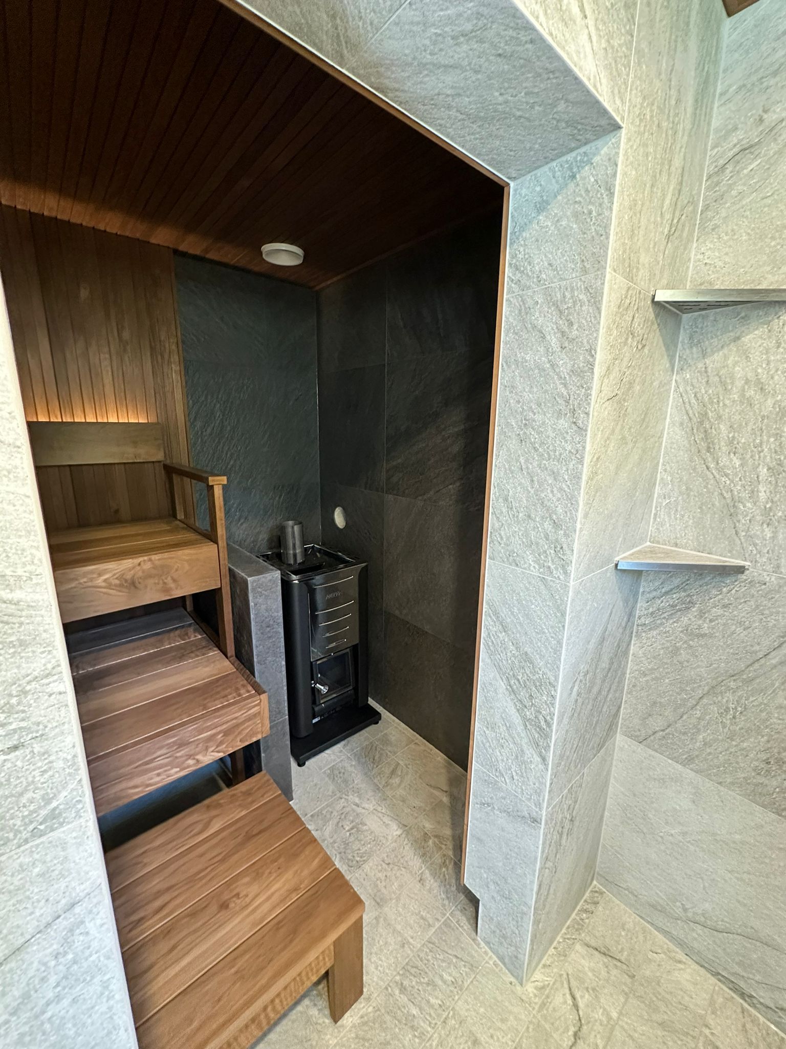 Saunaremontti ja kylpyhuone tumma paneeli lauteet ja integroitu kiuas Renomen Oy.
