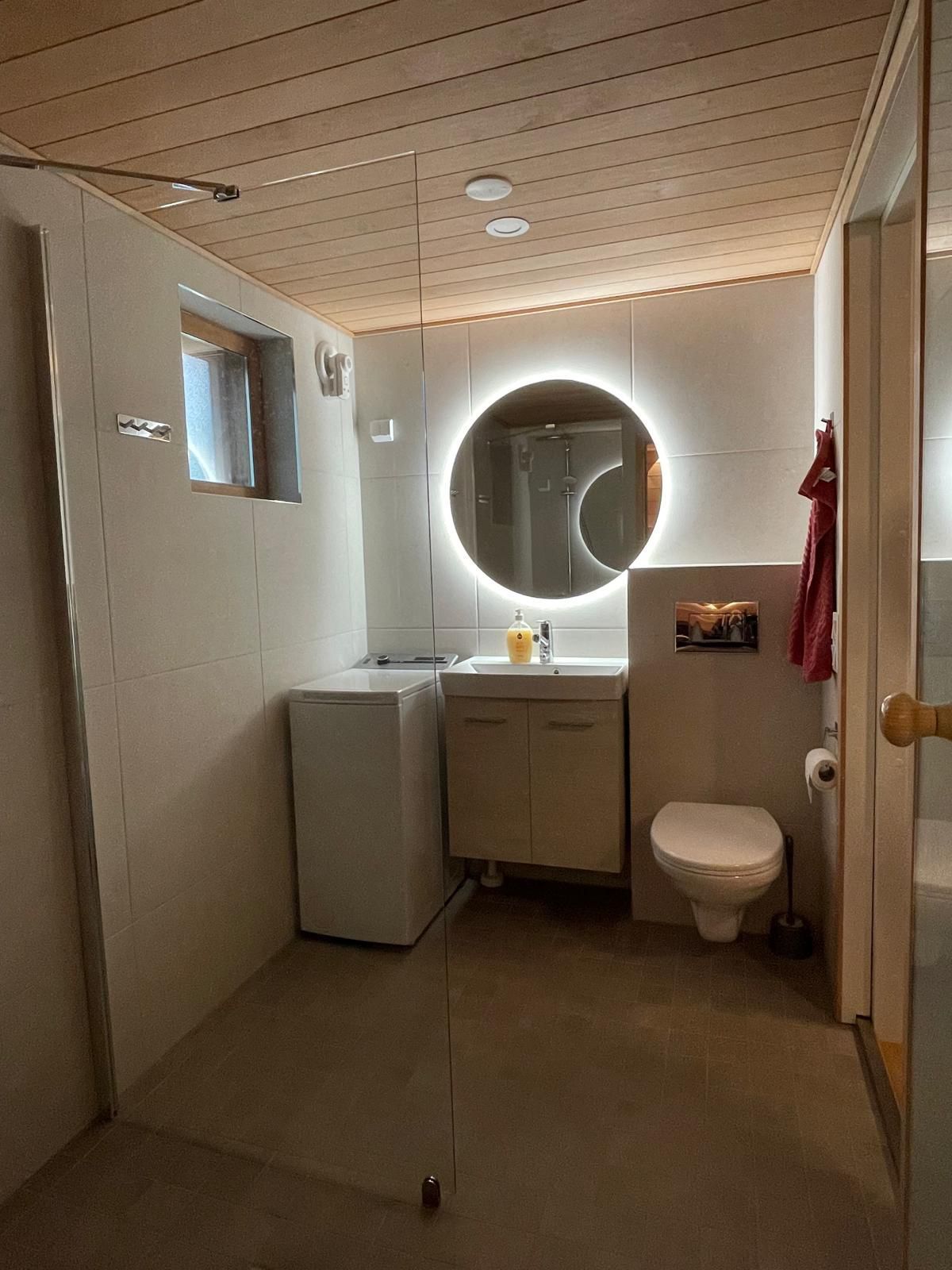 Renomen Oy kylpyhuoneremontti Uusimaa moderni pyöreä valopeili ja valkoinen allaskaappi.