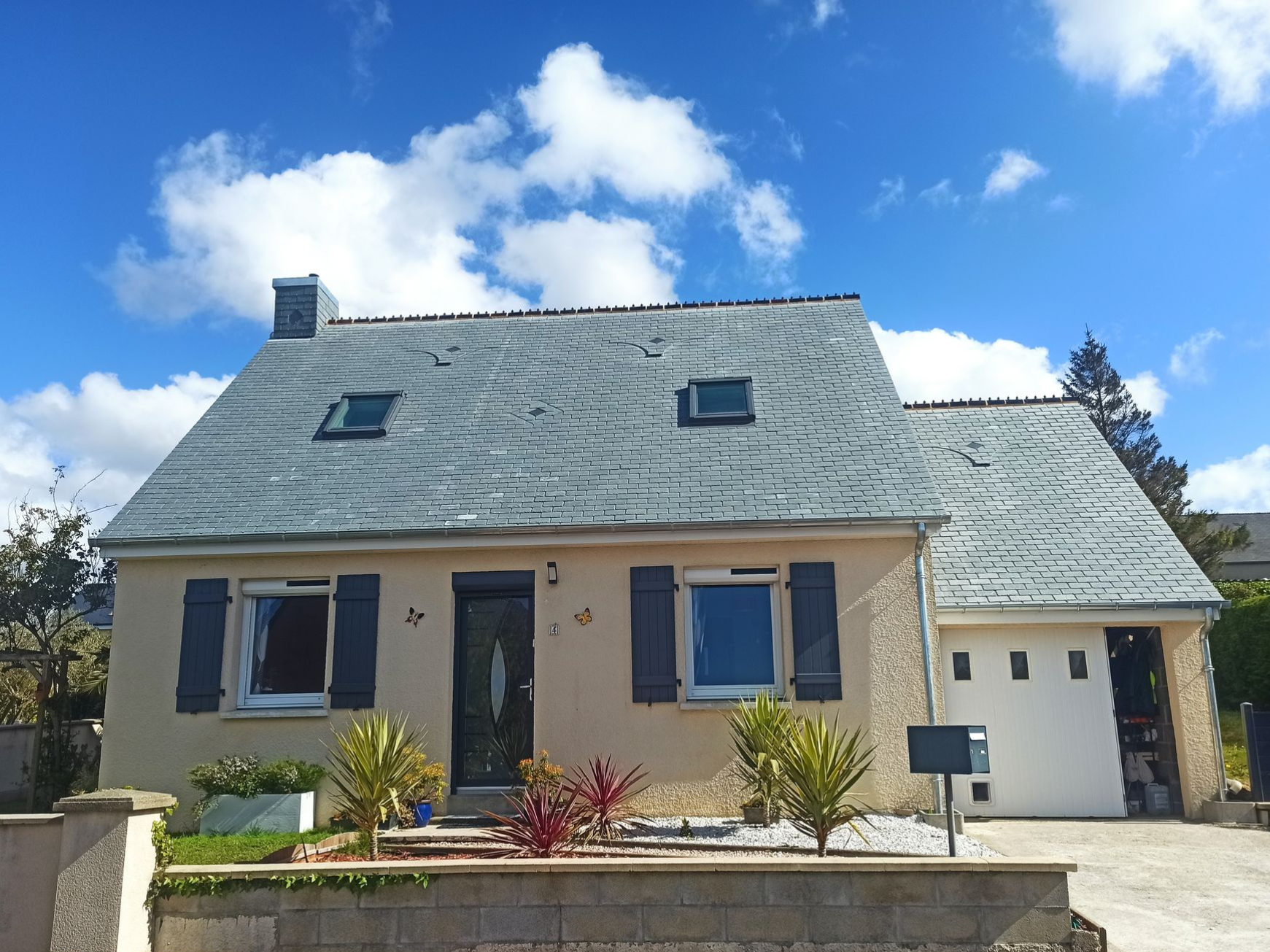 Maison beige de plain-pied avec toit gris, volets bleus et petit jardin devant