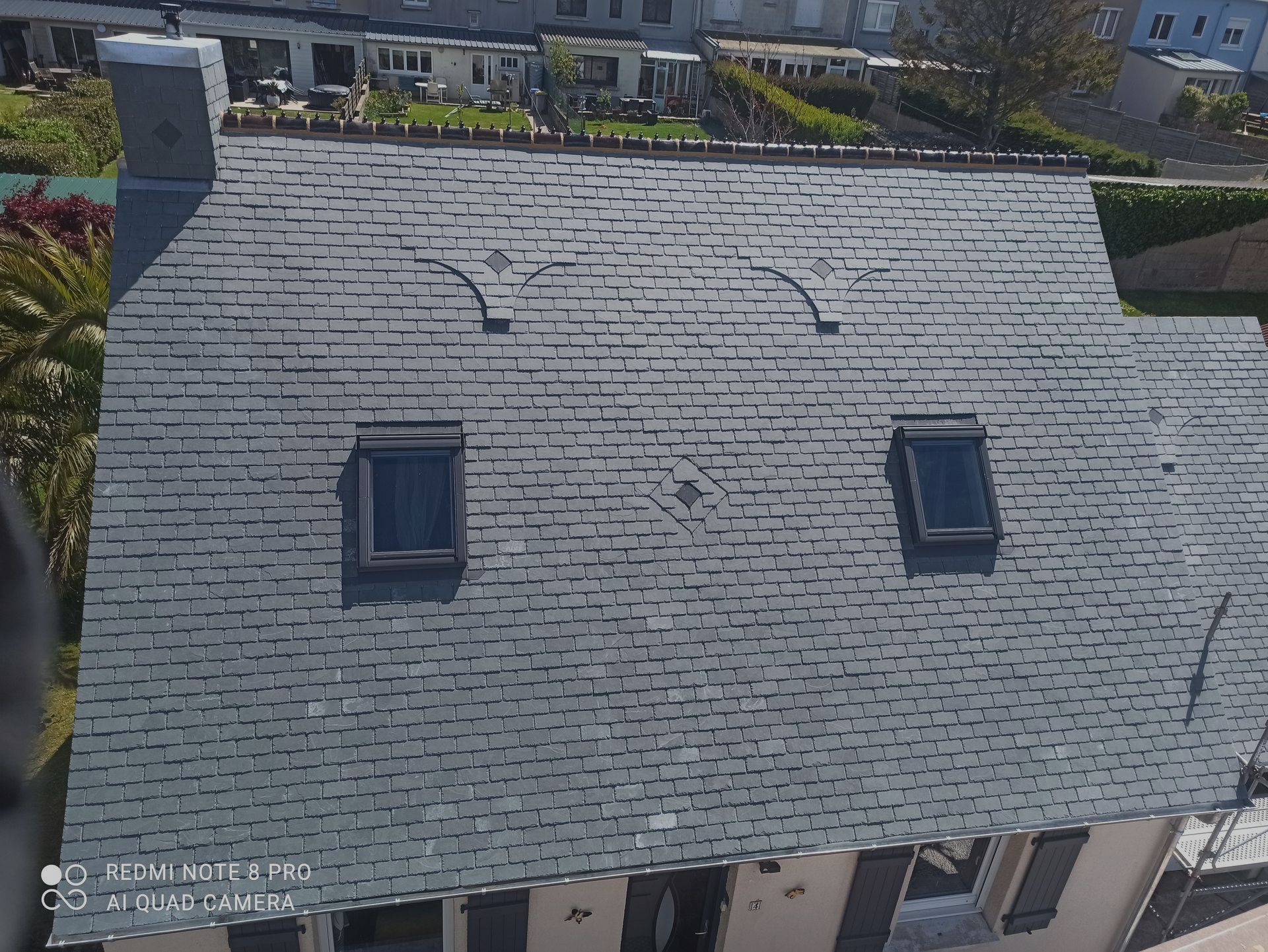 Vue aérienne d'une maison au toit d'ardoises grises, avec deux lucarnes et une cheminée