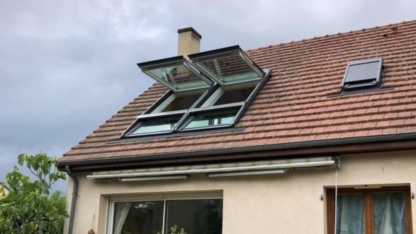 Fenêtre de toit encastrée dans une toiture zinc, avec des bâtiments en arrière-plan