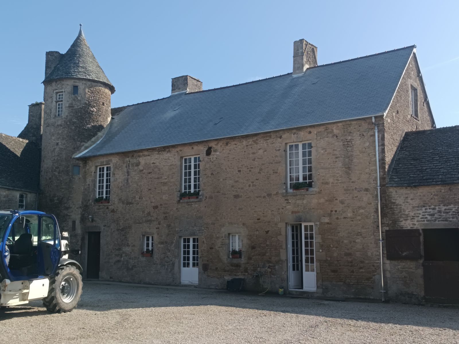 Ferme en pierre avec tourelle et tracteur bleu dans une cour ensoleillée