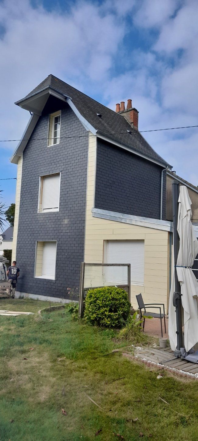 Grande maison à toiture en ardoise et bardage sous un ciel nuageux