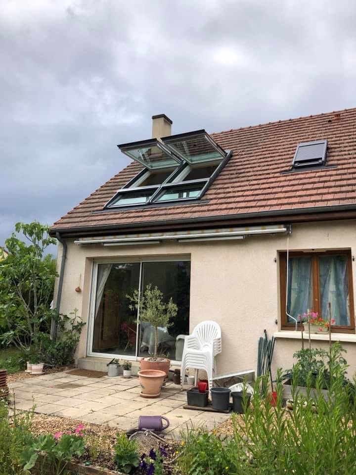 Petite maison beige au toit de tuiles, lucarnes, patio, plantes et chaises d'extérieur
