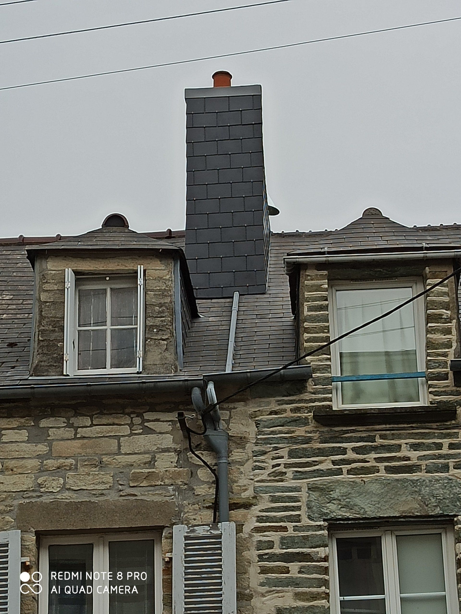 Toiture en ardoise d'une maison avec une haute cheminée centrale