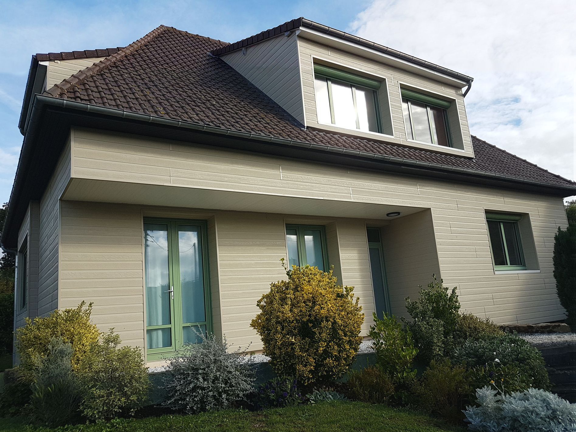 Maison moderne à deux étages avec bardage beige, toit de tuiles et jardin