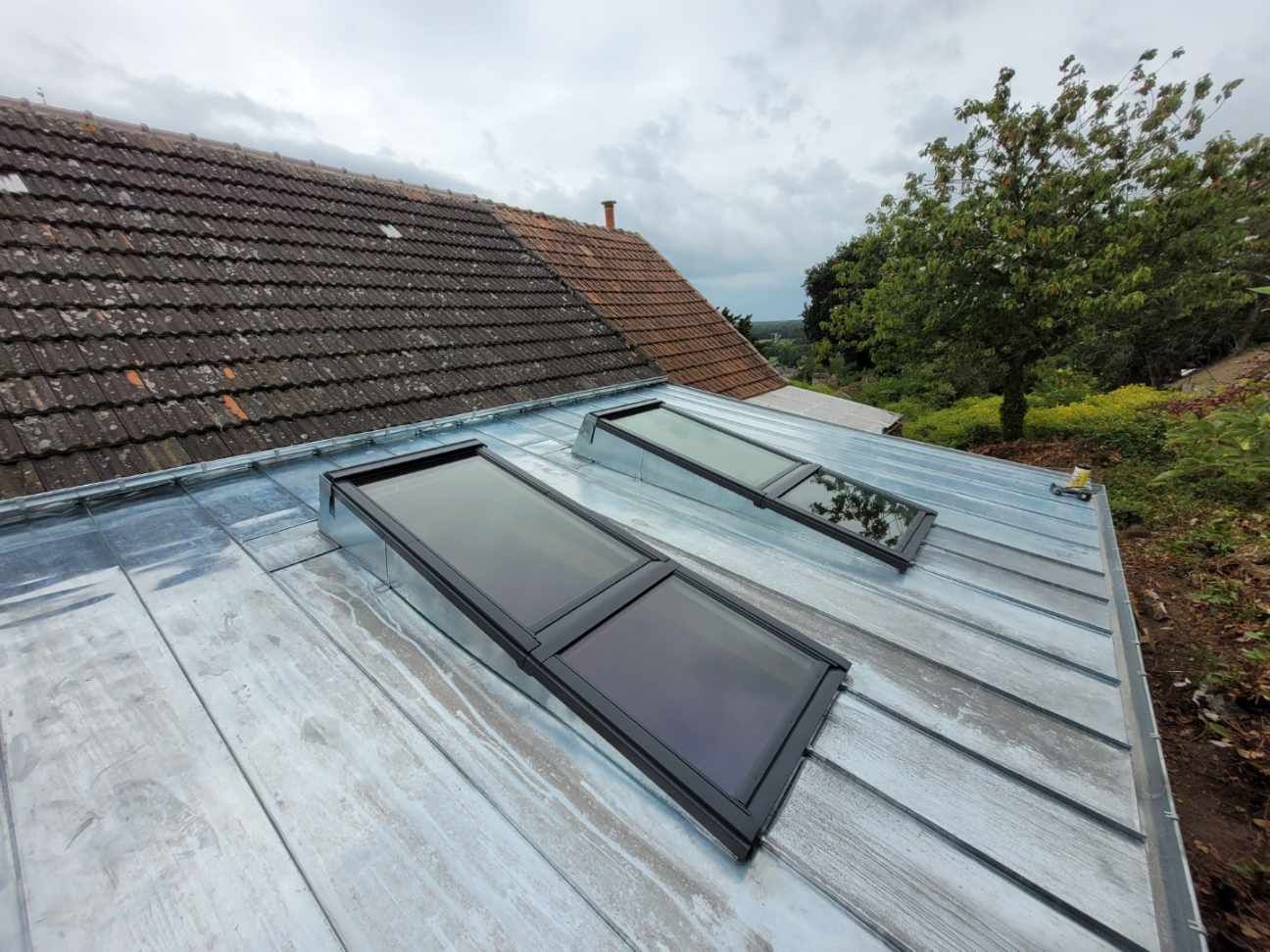 Deux puits de lumière sur une toiture métallique, à côté d'un toit de tuiles
