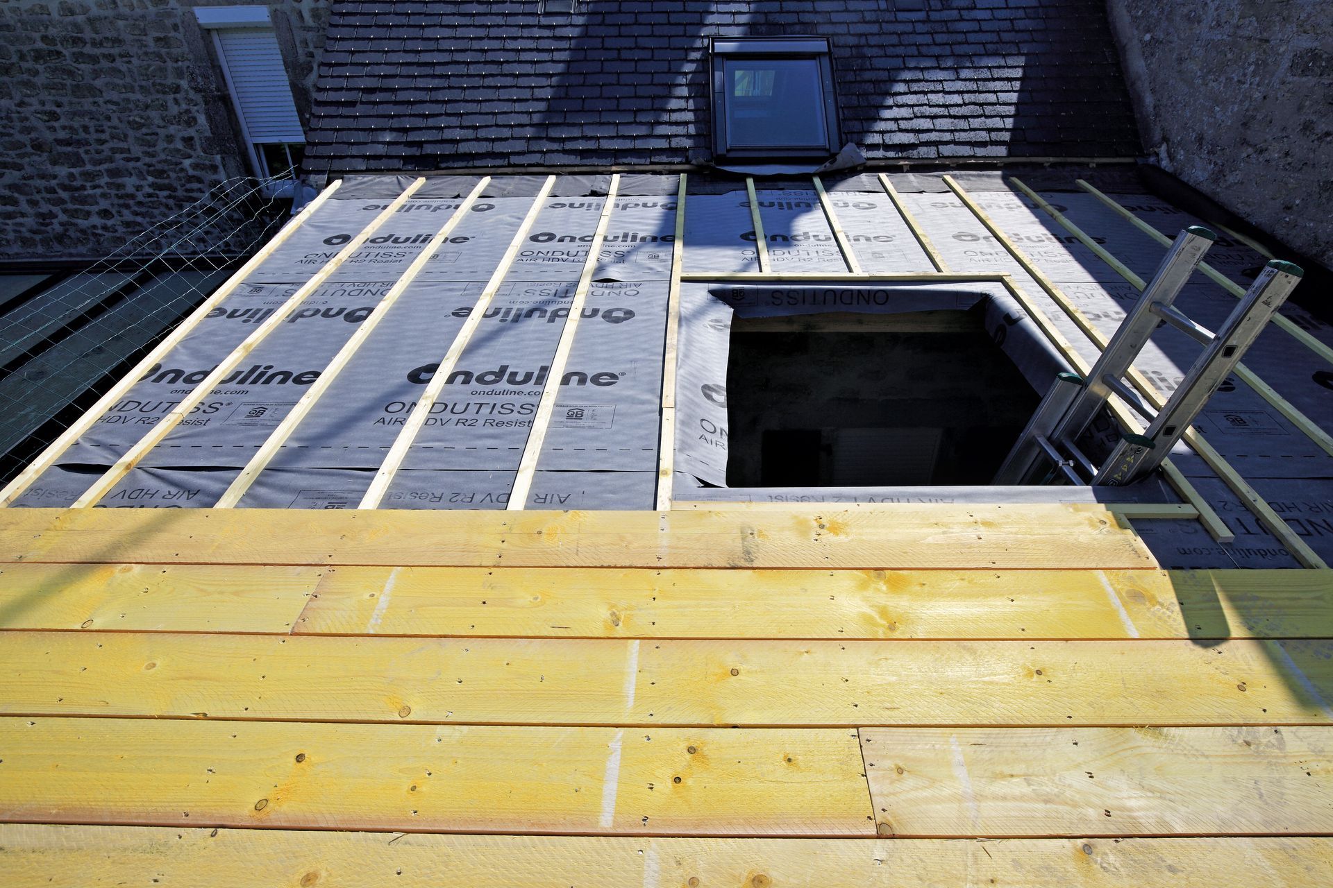 Toiture en construction avec voliges neuves, film sous-toiture et une échelle