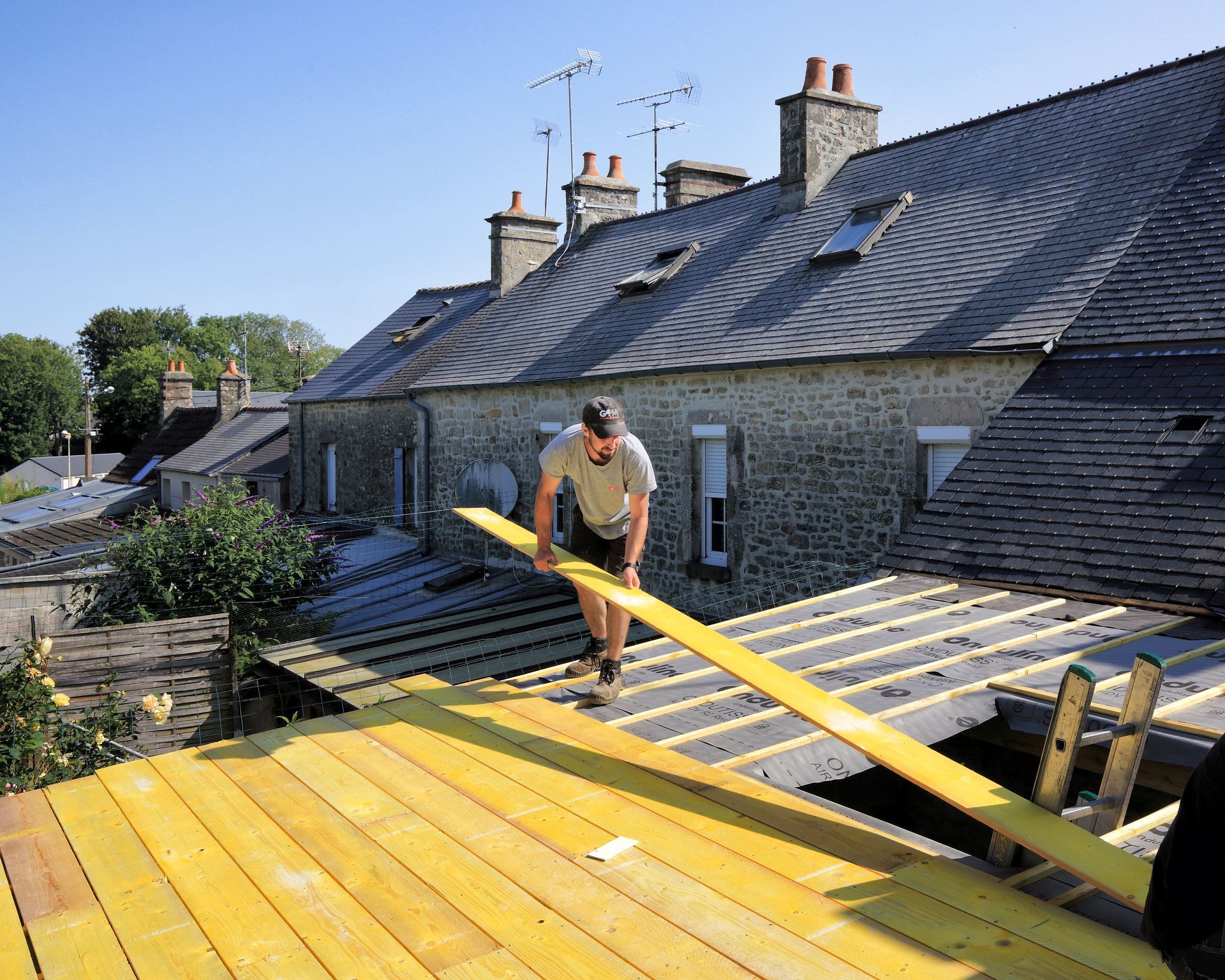 Un ouvrier installe des voliges sur le toit d'une maison par une journée ensoleillée