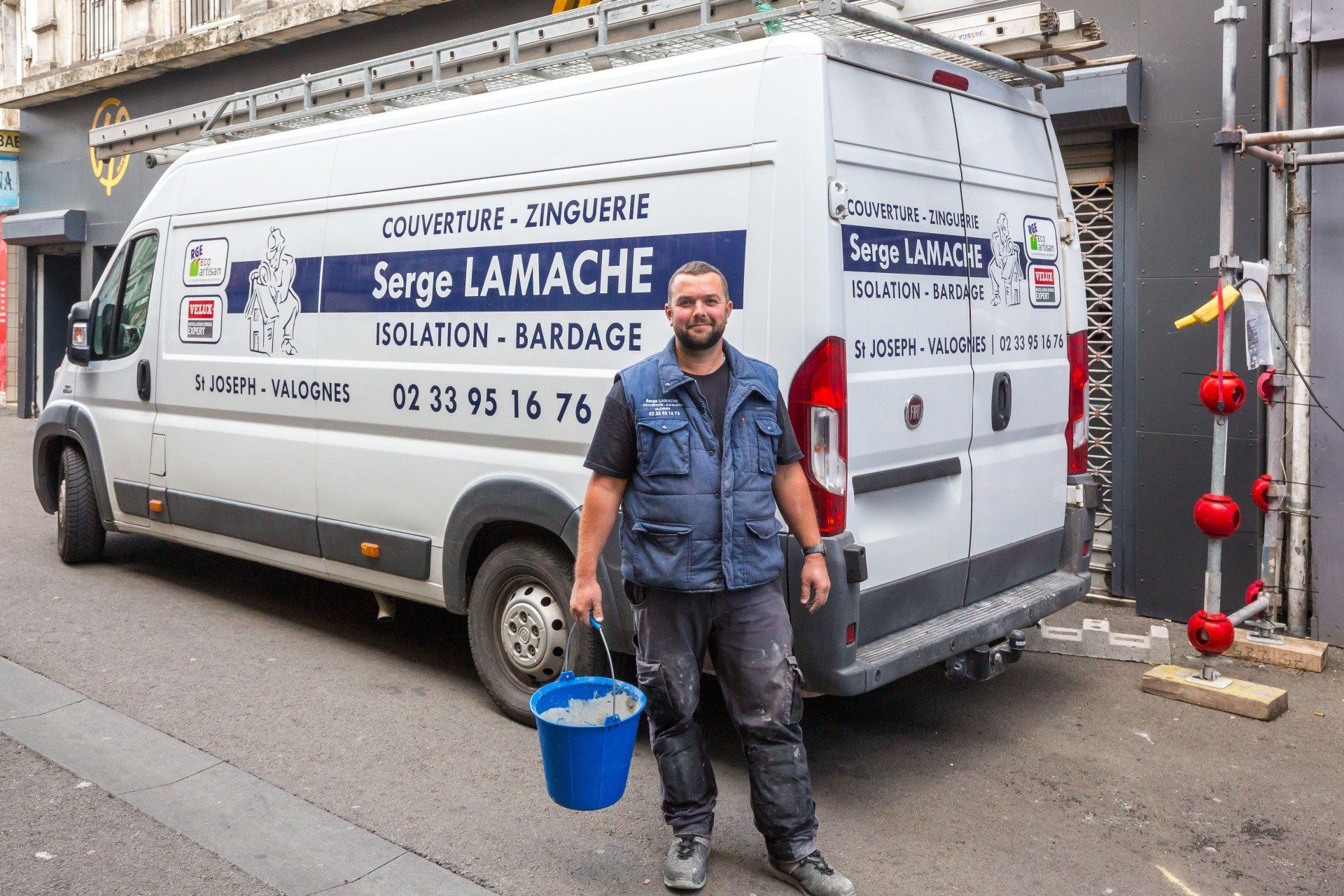 Un ouvrier tenant un seau bleu à côté d'une camionnette de service blanche garée dans la rue