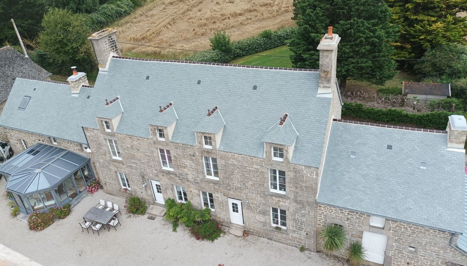 Vue aérienne d'une longue maison en pierre au toit d'ardoise avec une véranda à gauche