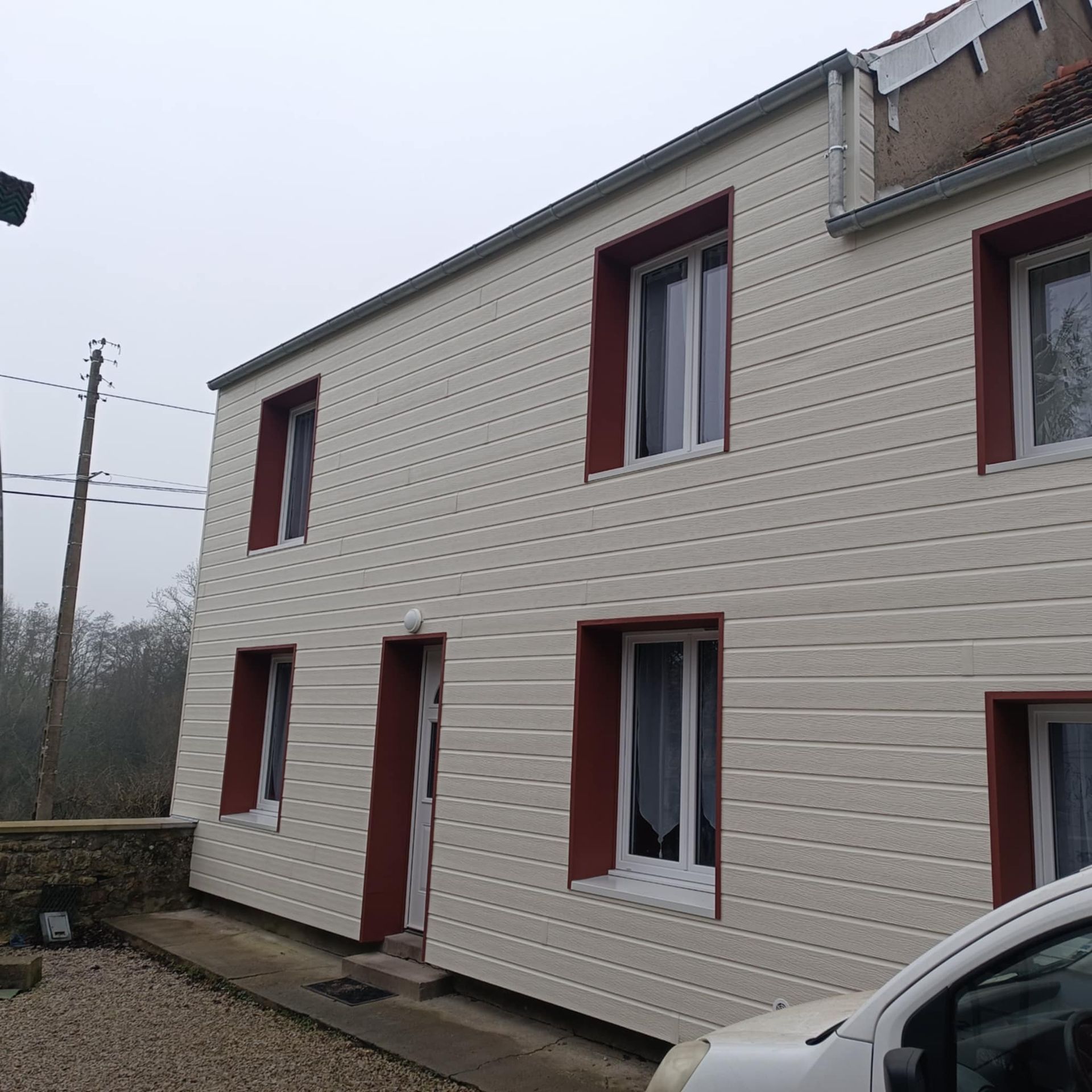 Maison à bardage beige et encadrement d'ouvertures en aluminium rouge