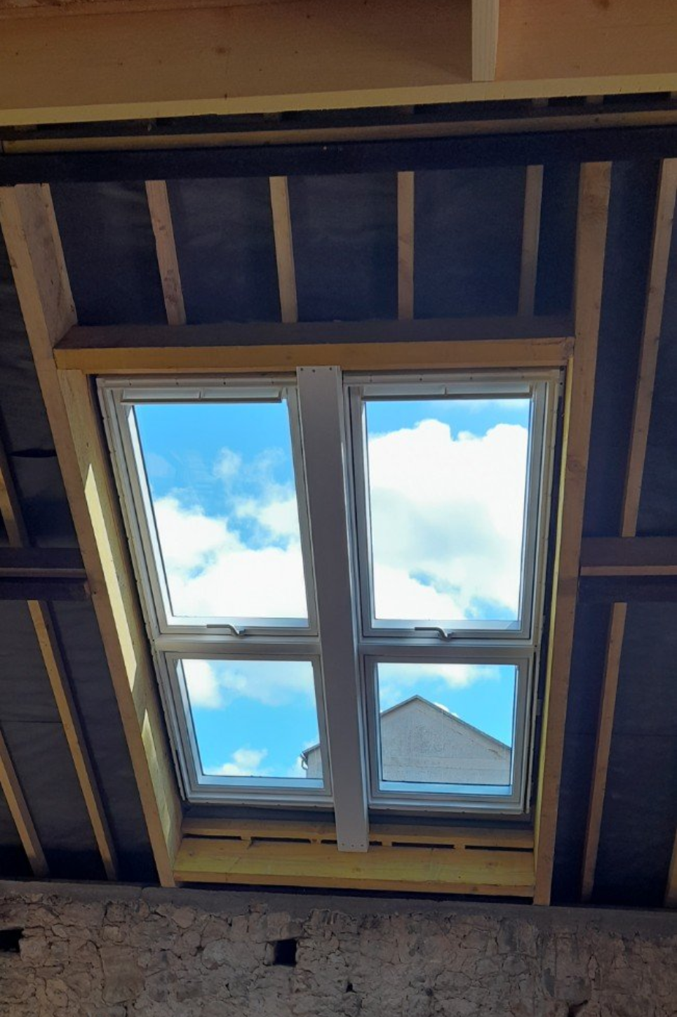 Fenêtre de toit dans un plafond incliné, laissant entrevoir un ciel bleu et des nuages