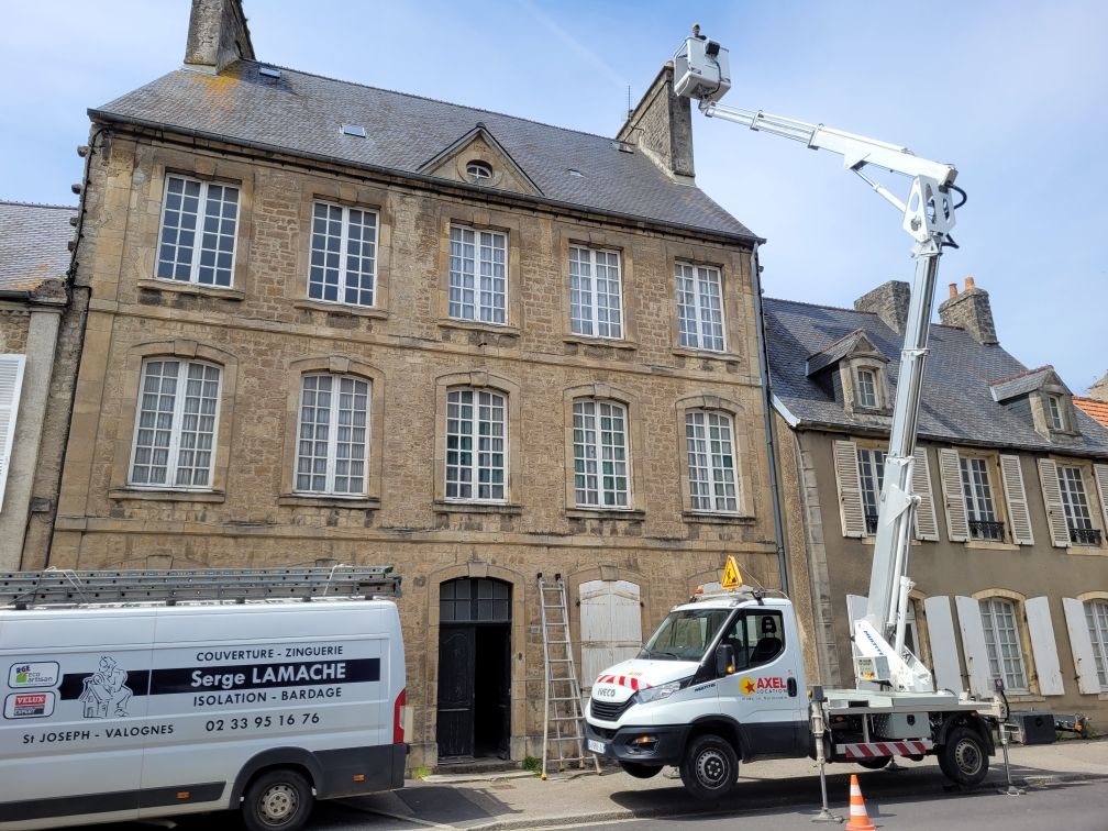 Immeuble en pierre avec deux camions et une nacelle élévatrice sur une rue pavée