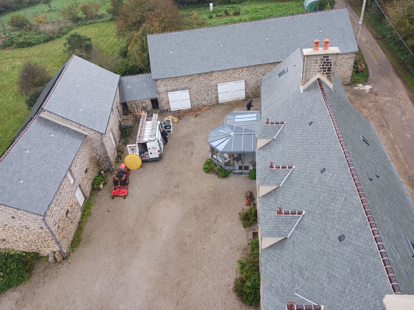 Vue aérienne d'une cour de ferme avec des bâtiments en pierre, des toits en ardoises neufs