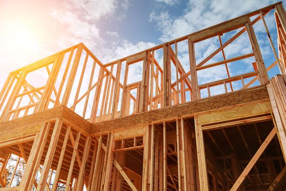 Charpente en bois d'une maison en construction se détachant sur un ciel lumineux avec un halo de soleil