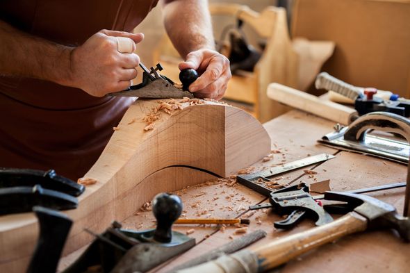 Des mains sculptent une pièce de bois sur un établi à l'aide de ciseaux à bois et d'outils de menuiserie.