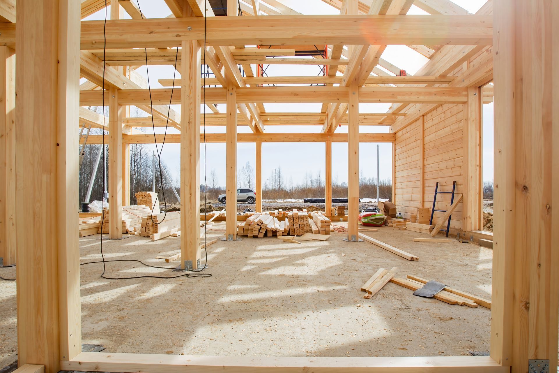 Charpente en bois d'une maison en construction, baignée de soleil, avec poutres apparentes, outils et débris au sol.