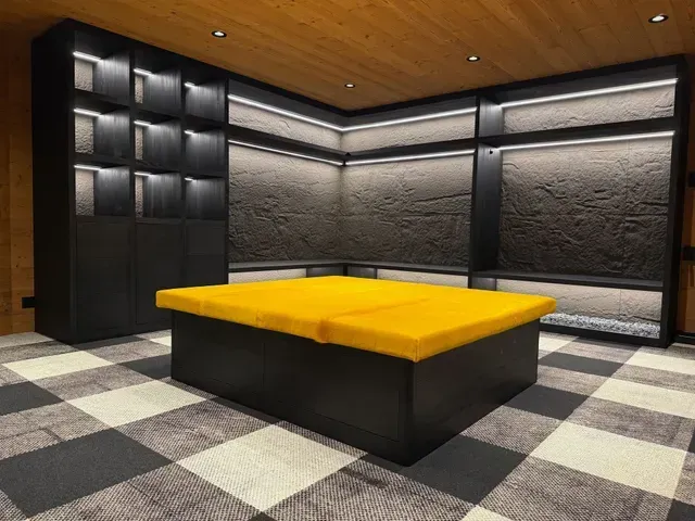 Chambre moderne vide avec murs noirs, sol à damier et un lit plateforme ou une banquette jaune au centre