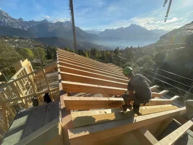 Ouvrier construisant une charpente de toit en bois avec vue sur un lac de montagne en arrière-plan