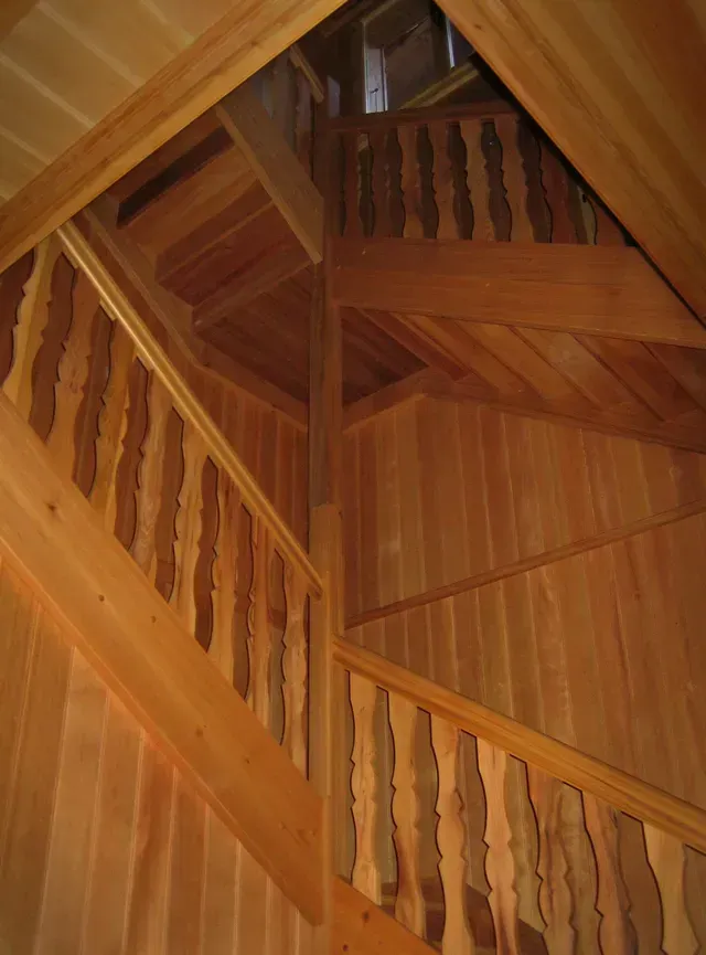 Escalier en bois à l'intérieur d'une cabane avec plafond voûté et balustrade, vu vers le haut