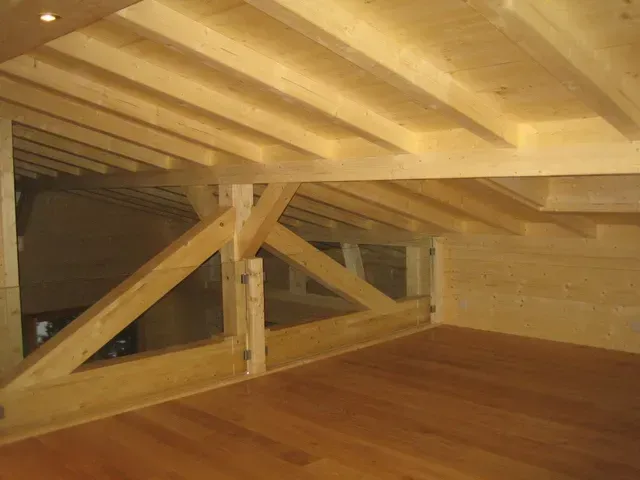 Grenier en bois avec poutres apparentes et contreventements sous un toit en pente, donnant sur un plancher en bois dur