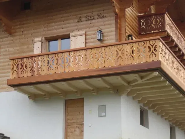 Balcon en bois sur une maison blanche avec balustrade sculptée et lanterne suspendue
