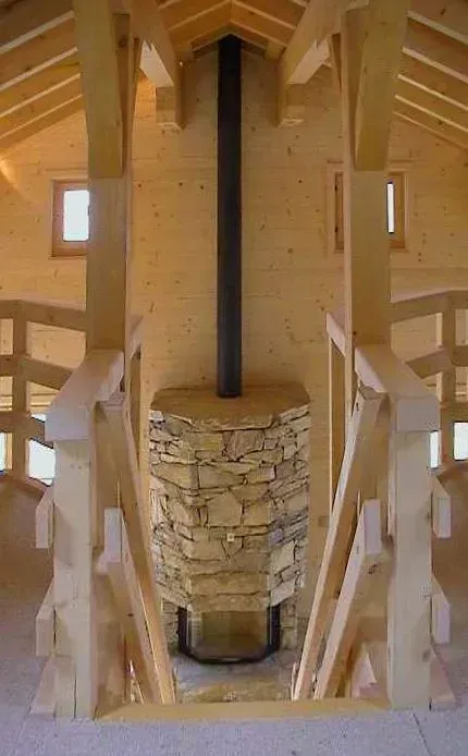 Escalier en bois avec cheminée centrale en pierre et conduit de cheminée noir dans un intérieur rustique