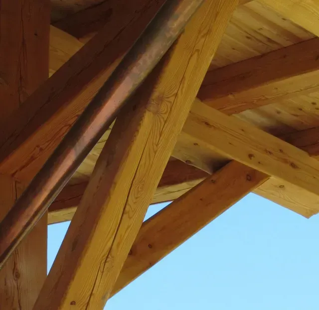 Poutres en bois et charpente du toit se détachant sur un ciel bleu clair.